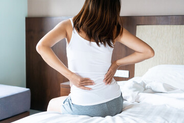 Back view of young Asian woman suffering from back ache on bed at home in the morning. close up