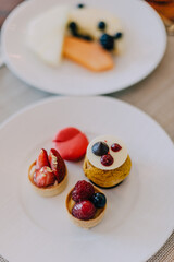 Plate with beautiful small desserts and cakes. Tartlets with strawberries, macaroon. All inclusive concept. Pastry in cafe.