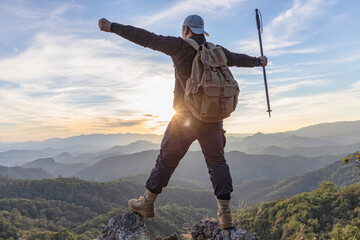 hiker with backpack at the top of a rock with his hands raised enjoy sunny day.Success concept.