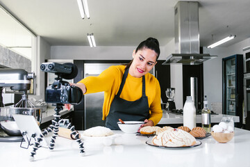 Latin Woman baking Conchas traditional Mexican bread while recording a video class with camera in a kitchen in Mexico city