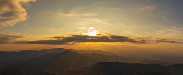 Panorama photo of sunset behind clouds on cliff with mountain hill forest and sunlight sunrays or sunbeams on background.
