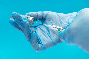 Hands in medical gloves taking dose of vaccine from glass vial. Close up.