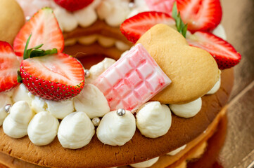 Sponge cake with strawberries, pink milk chocolate bars, silver sprinkles, vanilla cream and heart chape cookies close up. Summer sweet dessert for birthday or mothers day