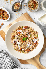 Homemade organic nut granola in a ceramic plate on a light background. Baked oatmeal muesli with almonds, walnuts, hazelnuts and pumpkin seeds top view