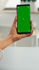 Business woman browsing on internet using mock up green screen chroma key smartphone sitting at office desk. Freelancer swiping online information for social media project using isolated device