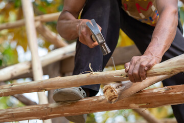 Close-up of a man hammering nails on a eucalyptus wood roof frame. House design using miniature eucalyptus