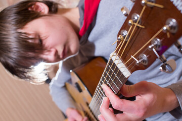 A young man plays the guitar. Selective focus on hand and strings. The model's face is out of focus.