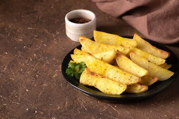 Country style potatoes. Baked potato wedges on a ceramic plate on a brown stone background with blank space on the left.