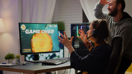 Stressed couple gamers losing space shooter video game playing on RGB powerful computer while streaming online competition. Pro cyber woman with headset performing from home during virtual tournament