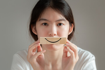Smile face symbol on wooden cube blocks. Asian woman holds a wooden block with a smiley symbol to express her feelings.