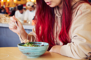 Cropped image of woman with red hair eating salad in a restaurant.
