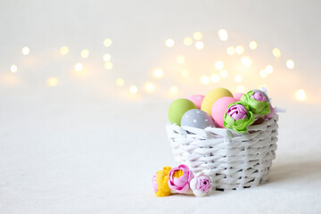 Fototapeta na wymiar A white wicker Easter basket with colorful eggs and bokeh lights in the background.