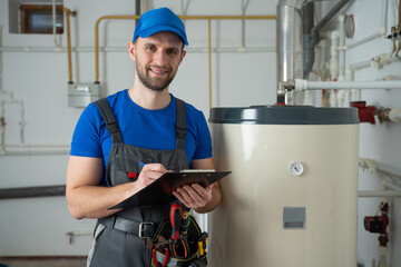 Technician servicing an hot-water heater. Man check equipment of the boiler-house - thermometer.  - obrazy, fototapety, plakaty