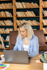 Focused young adult woman is using laptop, working on new business strategy. Concentrated female employee is sitting at the desk in home office, searching ideas, planning new project or startup