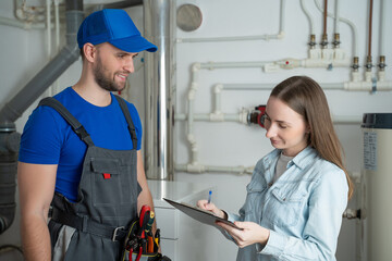 A female client signs a bill from a male plumber standing in the boiler room