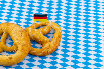 two pretzels decorated with the flag of Germany on a white and blue rhombus pattern background with copy space