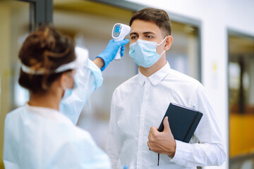 Disease control expert in visor and protective gloves with an Infrared thermometer equipment to check the temperature at office during pandemic. Covid-19. Temperature screening in quarantine.