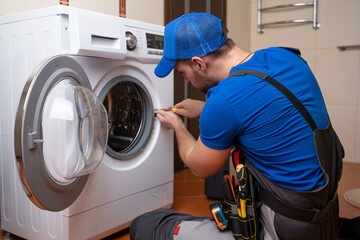 Working man plumber repairs a washing machine in home. Washing machine installation or repair....