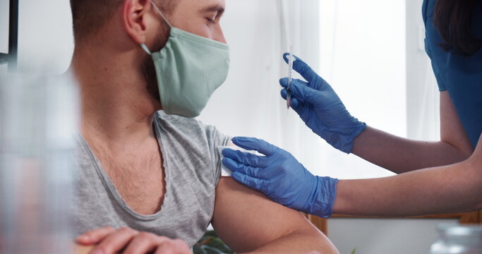 Vaccination Process. Young Nurse Doctor Woman In Blue Scrubs Gives Vaccine Injection Shot To Male Patient At Clinic.