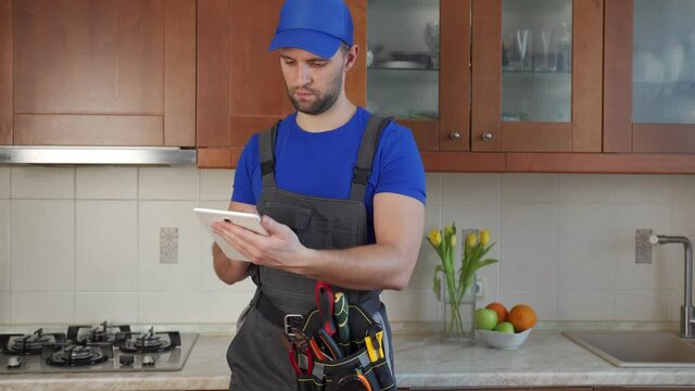 Plumber wearing a tool belt with various tools using tablet during work in kitchen