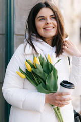 Portrait of a girl with tulips. The girl holds a paper cup with coffee in her hands.