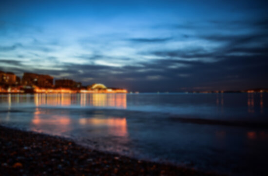 Defocused winter landscape. Cloudy evening view of the bright lights of the buildings and the city center of the resort of Gelendzhik from the sandy beach. Russia, Black sea coast