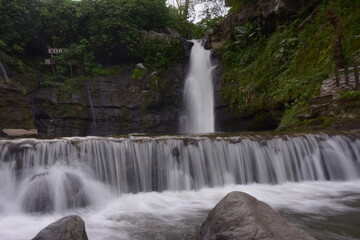 A stunning jungle waterfall flows into a cool mountain river with big rocks.