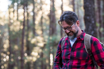 Man hiking and enjoying in a woods forest location. Side view of a man wearing a bag walking through a forest. Happy adult young caucasian male portrait enjoying healthy nature lifestyle outdoor