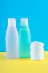 Two cosmetic bottles with micellar water and cotton pads. Facial skin care concept. Yellow and blue paper background. Makeup remover. Face toner, skin cleanser. Daily care, cleansing. Beauty product.