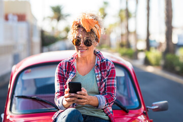 Trendy female young adult caucasian woman use modern phone connection outdoor near her pretty red...