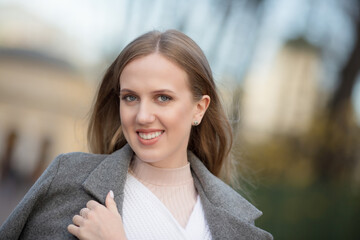 Portrait of a beautiful young woman in a gray coat. An attractive woman with light brown hair walks...