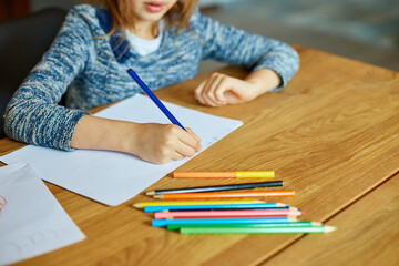 School girl drawing and writing a picture with crayons, using colored pencils