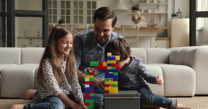 Loving dad play blocks with little son and daughter spend time together sit on warm floor in living room construct tower use colorful plastic cubes toys set. Quarantine time with kids leisure concept