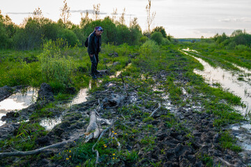 Woman near blurred water forest road. Woman hiker in the spring visits the swamps. Due to the spring flood, it is difficult to walk on a dirt road.