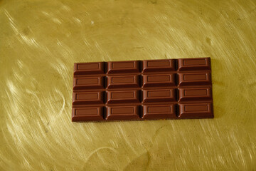 Chocolate bar on a gold metal background. Copy space.