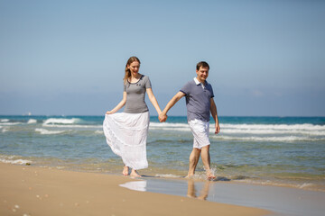 Fototapeta na wymiar Young man woman on sea vacation. Couple funny run on a tropical beach at sunny day, enjoying summer holidays. Summer lifestyle portrait of pretty young lovers. Vacation travel in tropic country
