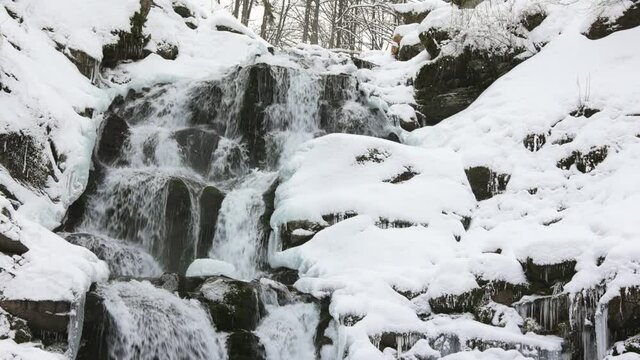 Small mountain streams of icy water flow among wet stones covered with white snow, and 3x slow-mo