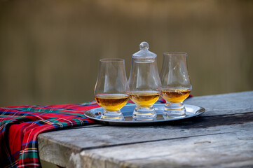 Tasting glasses of scotch whisky strong drink and red Scottisch tartan on old outdoor table
