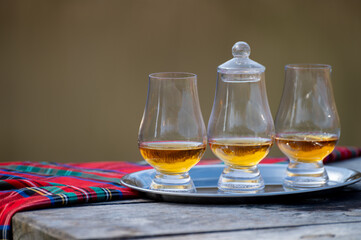 Tasting glasses of scotch whisky strong drink and red Scottisch tartan on old outdoor table