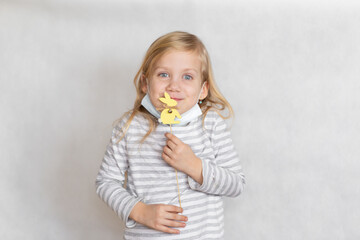 blonde girl with a small shepherd's egg in hand, Easter, girl in striped jacket, girl with blue eyes girl in a mask on a light background, holding an Easter bunny in her hands