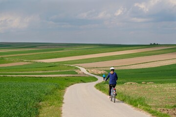 Silhouettes of cyclists on a winding road between beautiful colored fields situated on the hills