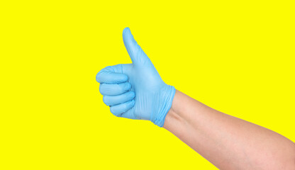 Thumbs up in a blue latex glove on a yellow background.