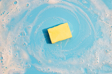 Dishwashing sponge with foam on blue background.