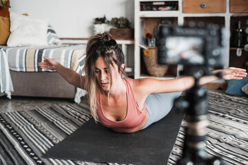 Young woman exercising at home doing pilates and recording at her with digital camera to teach workout and produce web class - content creator business free healthy lifestyle people concept