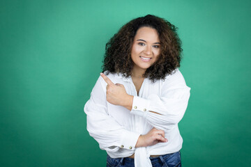 Young african american girl wearing white shirt over green background smiling and pointing with hand and finger to the side