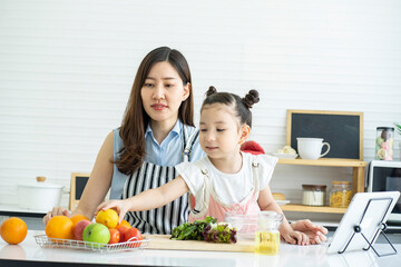 A cute daughter picks up an orange, prepares a salad, talks to the mother, and she takes a cooking class through the internet in the kitchen. 
