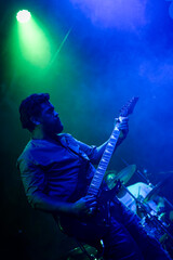 Musician playing electric guitar during rock band live concert. Black hair male guitar player performing on stage. Music foggy lights show
