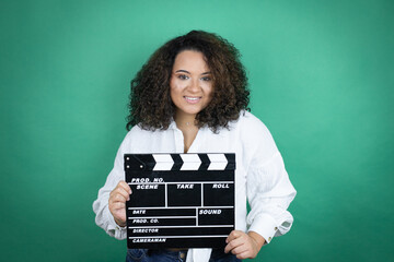 Young african american girl wearing white shirt over green background holding clapperboard very...