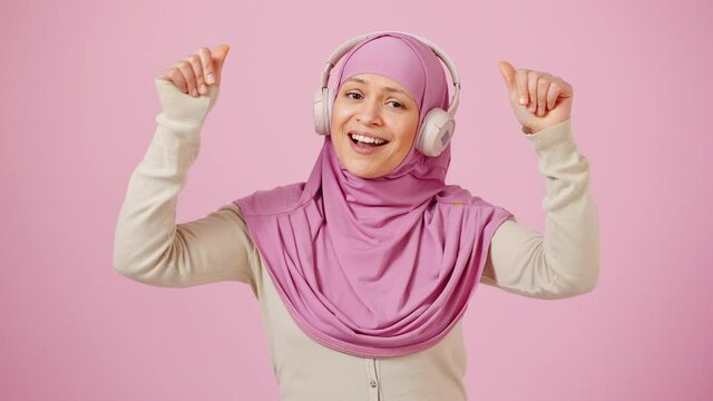 Music lover. Energetic middle aged muslim woman enjoying great sound of wireless headphones and dancing traditional pas