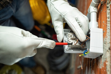View from above. Electrician worker at work with a screwdriver fixes the cable in the terminal of the switch of a residential electrical system. Working safely with protective gloves. Construction ind - obrazy, fototapety, plakaty